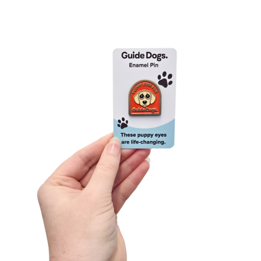 Image of a Guide Dogs enamel pin on a card held by a hand against a white background