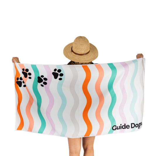 Image of person holding a colorful towel with wavy patterns and Guide Dogs logo.