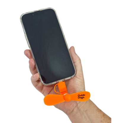Image of a hand holding a smartphone with an orange fan labeled 'Guide Dogs' inserted into the basee on a white background