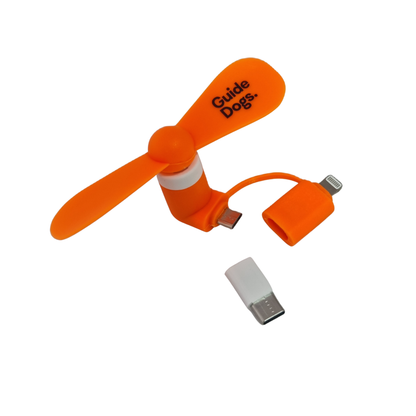 Image of an orange Phone Fan labeled Guide Dogs with detachable USB-C and Lightning adapters for your phone.