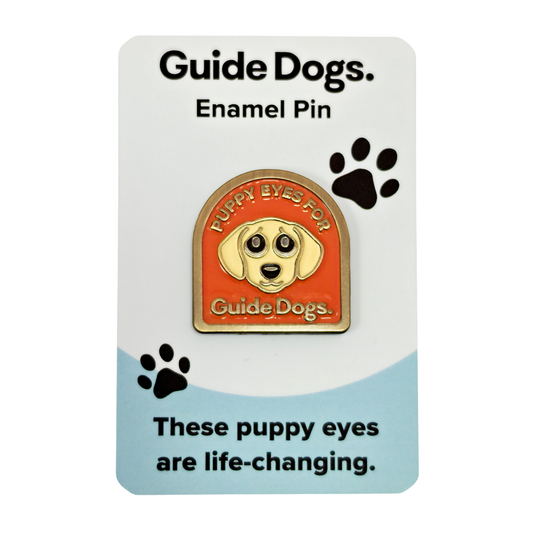 Image of Enamel Pin with a dog face and puppy eyes for Guide Dogs, mounted on an orange paw print card.