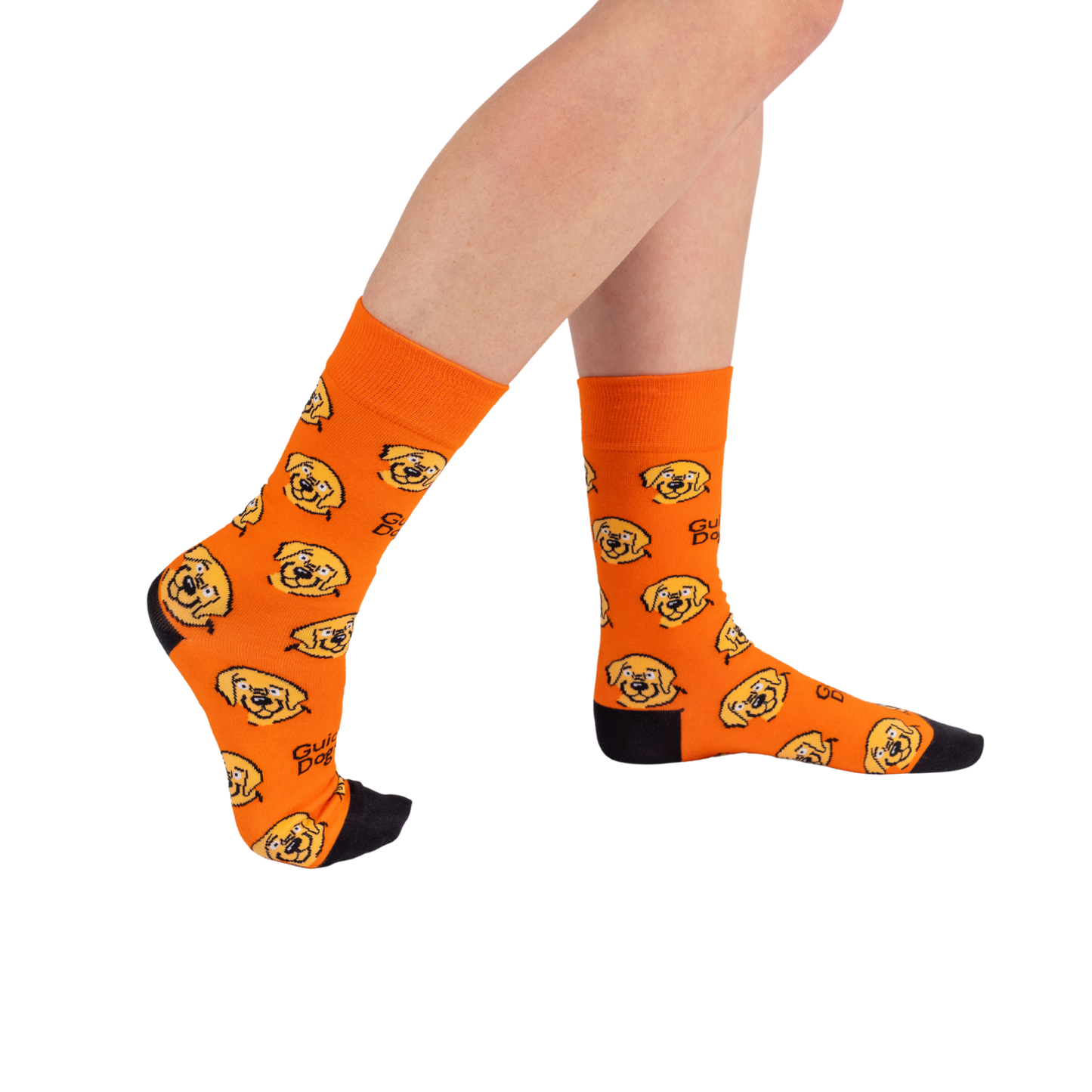 Image of Person wearing bright orange Socks - Coloured with cartoon dog faces, black toes and heels, legs crossed on white background.