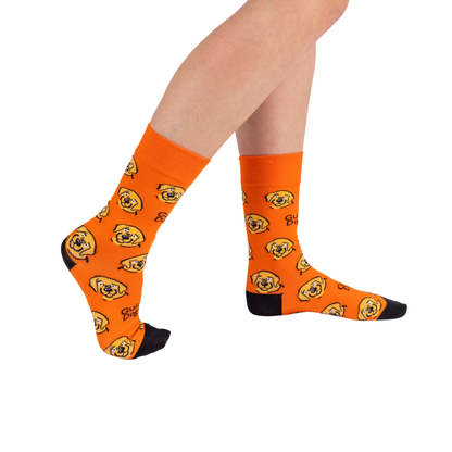 Image of Person wearing bright orange Socks - Coloured with cartoon dog faces, black toes and heels, legs crossed on white background.