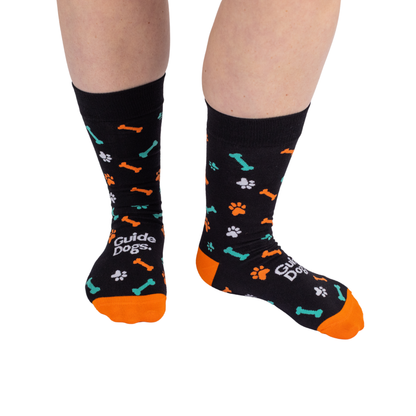 Image of Adult Socks - Coloured: black with orange toes, bones, paw prints & Guide Dogs text; fits adult foot sizes.