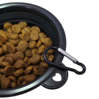 Image of a close-up of a black collapsible pet bowl filled with brown kibble, with a black carabiner clipped to the rim against a white background.