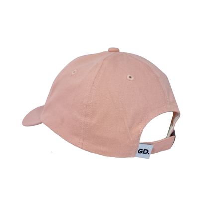 Image of A light pink Caps hat shown from the back with an adjustable strap and a small white “GD” tag.