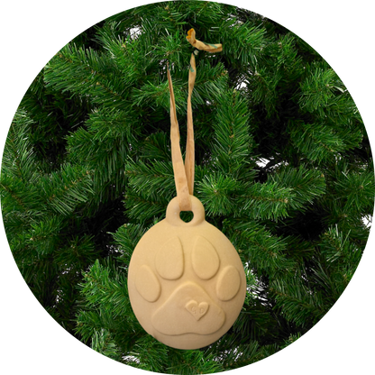 Image of Christmas Ornaments with paw prints hang from ribbons on a green artificial Christmas tree.