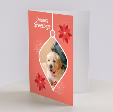Image of a red card with golden retriever puppy and poinsettias by the Christmas tree.