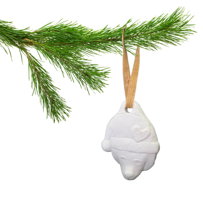 Image of A pine branch displays a Christmas Ornament: a white bear head with Santa hat and brown ribbon.