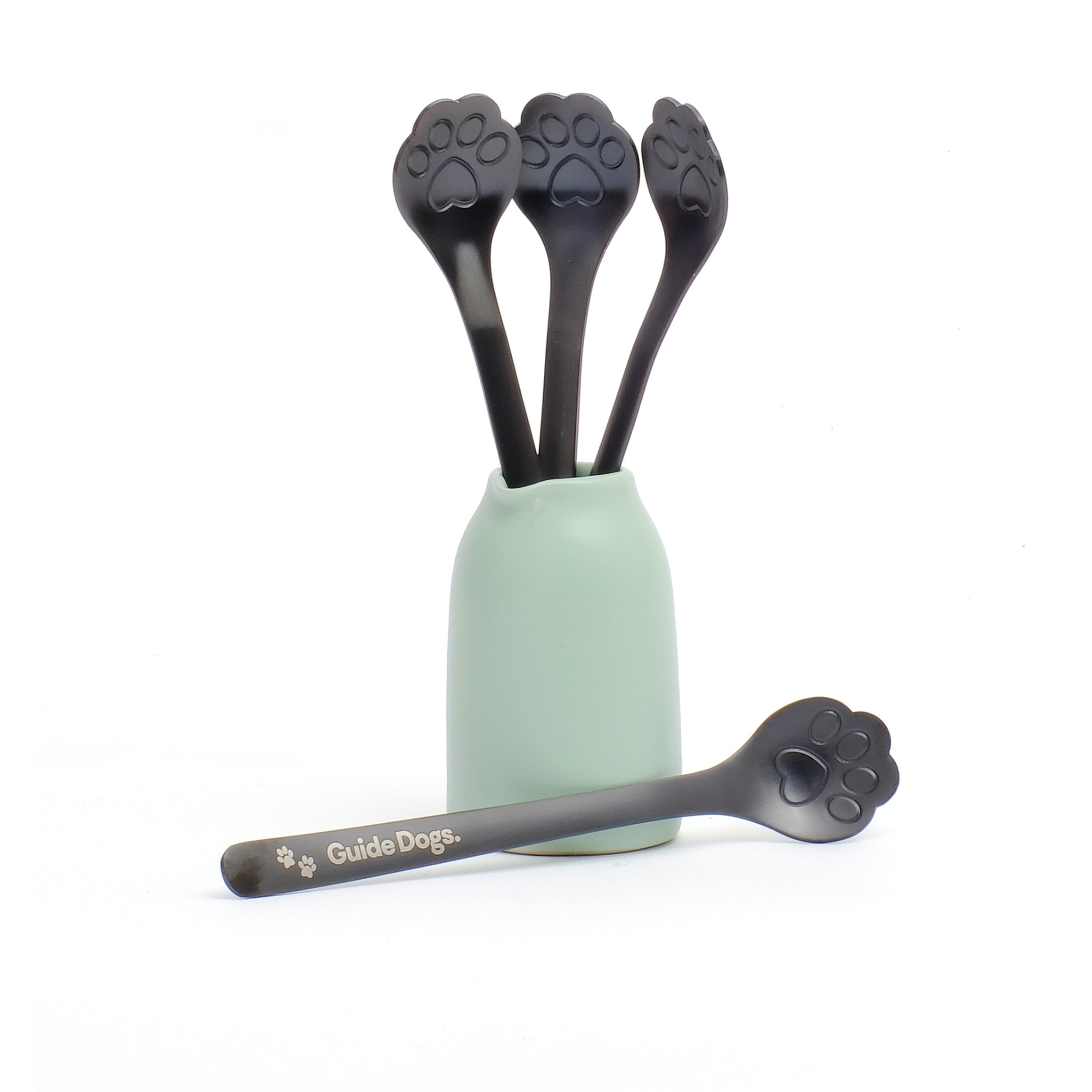 Image of The Paw Spoon - Black set includes four spoons in a mint green holder, one labeled "Guide Dogs" for dog breakfasts.