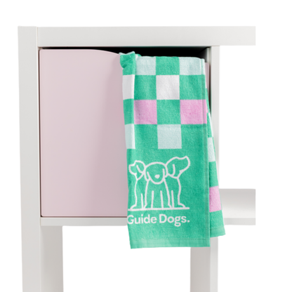 Image of A Tea Towel- Puppy Icons (2 pack) with green and pink checkers hangs on a white and pink cabinet.