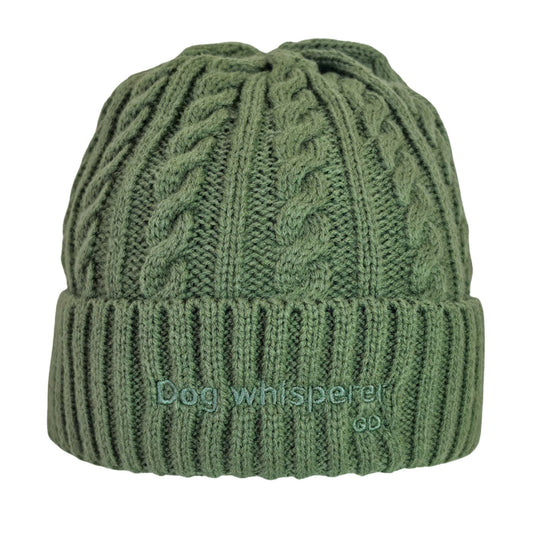 Image of an olive green cable-knit beanie hat with a ribbed cuff, featuring the embroidered text 'Dog whisperer' on the front, set against a plain white background