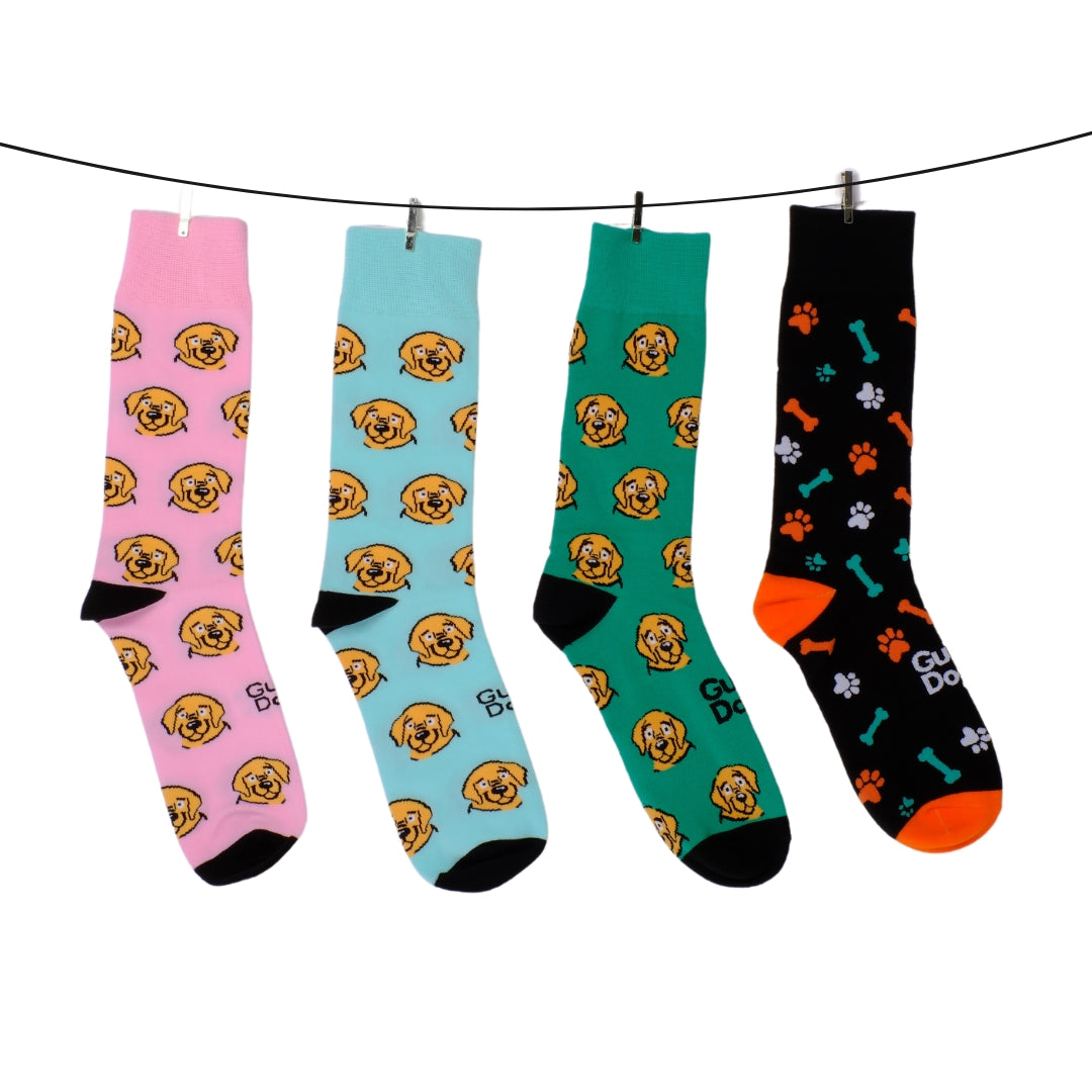 Image of a four pairs of socks with dog-themed designs hang on a clothesline. The first three feature beige dog faces and the socks are pink, blue and green; the fourth is black with paw prints, bones, and orange accents. 