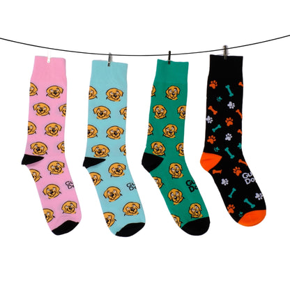 Image of a four pairs of socks with dog-themed designs hang on a clothesline. The first three feature beige dog faces and the socks are pink, blue and green; the fourth is black with paw prints, bones, and orange accents. 