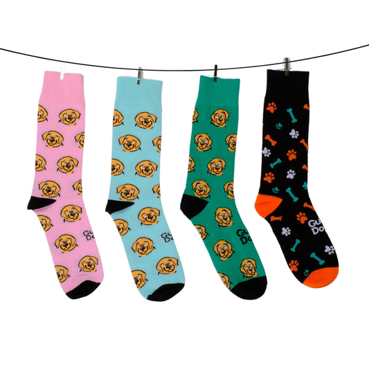 Image of a four pairs of socks with dog-themed designs hang on a clothesline. The first three feature beige dog faces and the socks are pink, blue and green; the fourth is black with paw prints, bones, and orange accents. 
