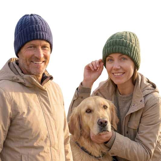 Image of a smiling man and woman wearing knit beanie hats and beige jackets pose with a golden retriever dog against a bright white background.