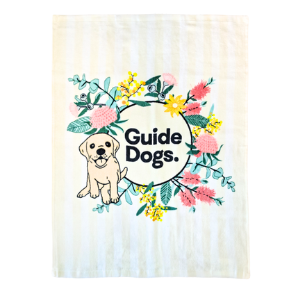 Image of a cream and white tea towel with  Guide Dogs logo and a dog illustration with floral elements on a white background.