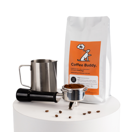 Image of Soho Coffee and Hot Chocolate with metal milk jug, tamper, portafilter, and scattered coffee beans on white surface.