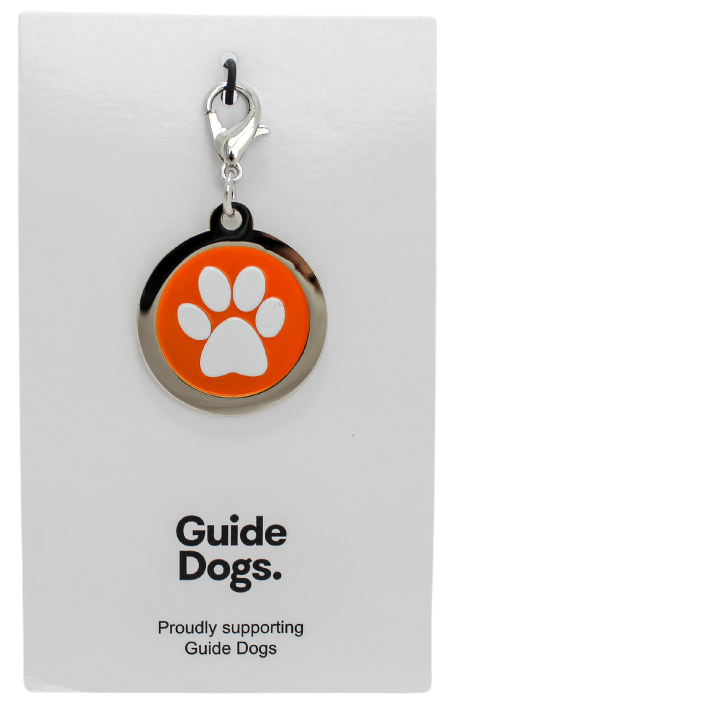 Image of a round metal charm with a white paw print on an orange background. on a card reading Guide Dogs.