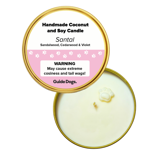 Image of top view of a gold candle tin  featuring a paw-shaped wax detail at the centre, a lid labeled “Santal” scent, and text 'Warning - May cause extreme cosiness and tail wags!
