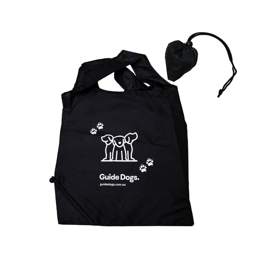Image of a black shopping bag with white Guide Dogs logo and paw prints, includes matching drawstring pouch.
