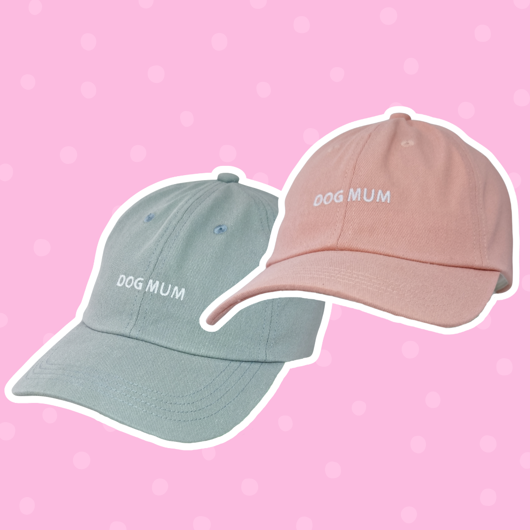 Image of two caps—one light blue, one pink with 'Dog Mum' embroidered above the brim.