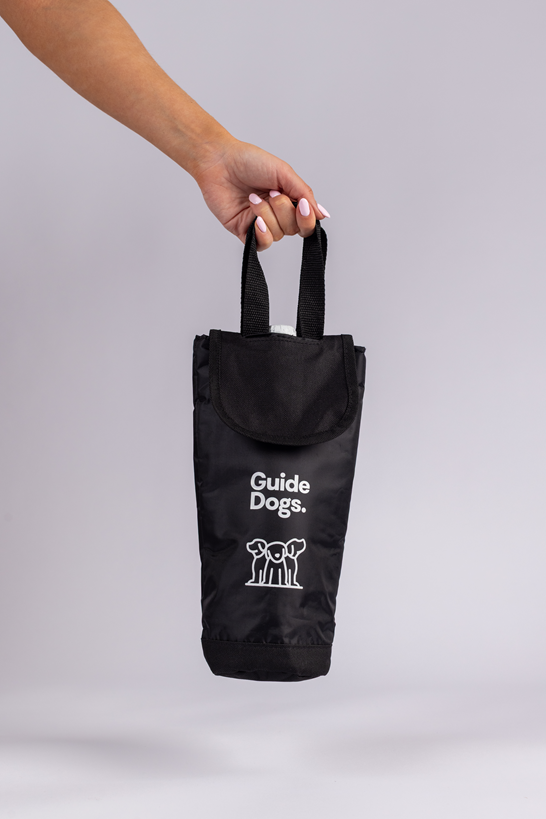 Image of a hand holding a black Wine Cooler Bag, featuring two handles, the Guide Dogs logo, and two white dog illustrations on the front. 