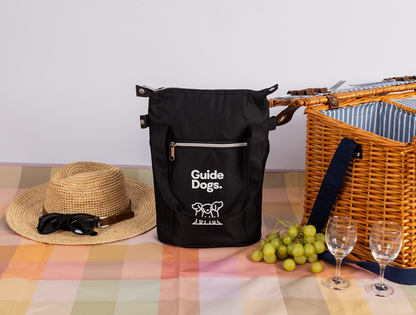 Image of a Wine Cooler Bag, placed on a picnic rug with a wicker picnic basket, green grapes, and two empty wine glasses.