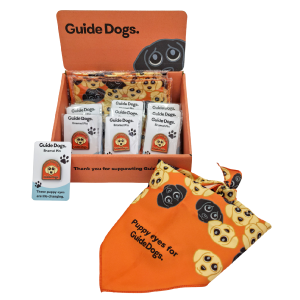 Image of Starter Fundraising Box display with dog-themed bandanas, pin badges, and a 'Puppy eyes for Guide Dogs' sign.