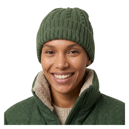 Image of a smiling woman wearing a dark green ribbed knit beanie and a matching green fleece jacket with a beige sherpa-lined collar, photographed against a plain white background.