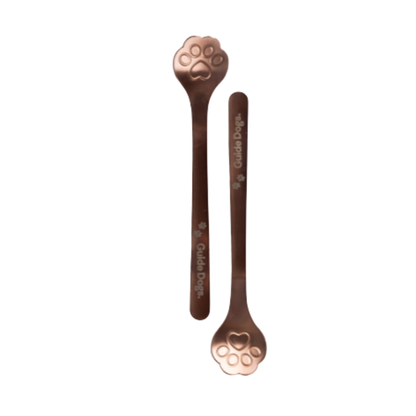 Image two metallic rose coloured spoons with paw print shape bowls and Guide Dogs written on the handle.