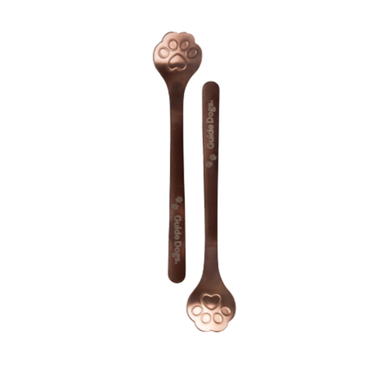 Image two metallic rose coloured spoons with paw print shape bowls and Guide Dogs written on the handle.