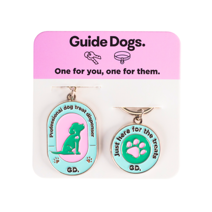 Two dog-themed keychains on a Guide Dogs packaging with pink and white background.